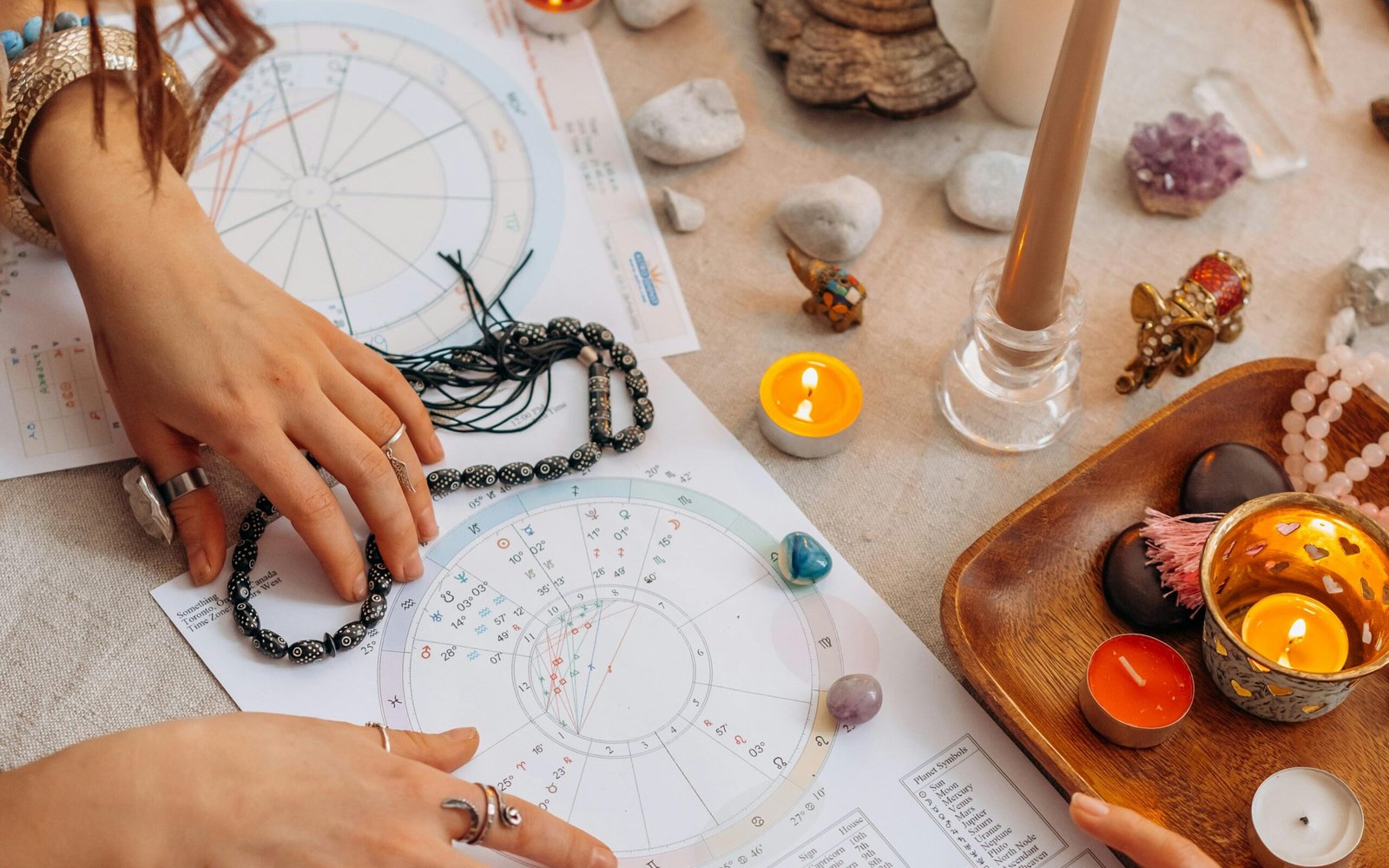 Hands arranging astrology charts with candles and crystals on a table for a spiritual ritual.